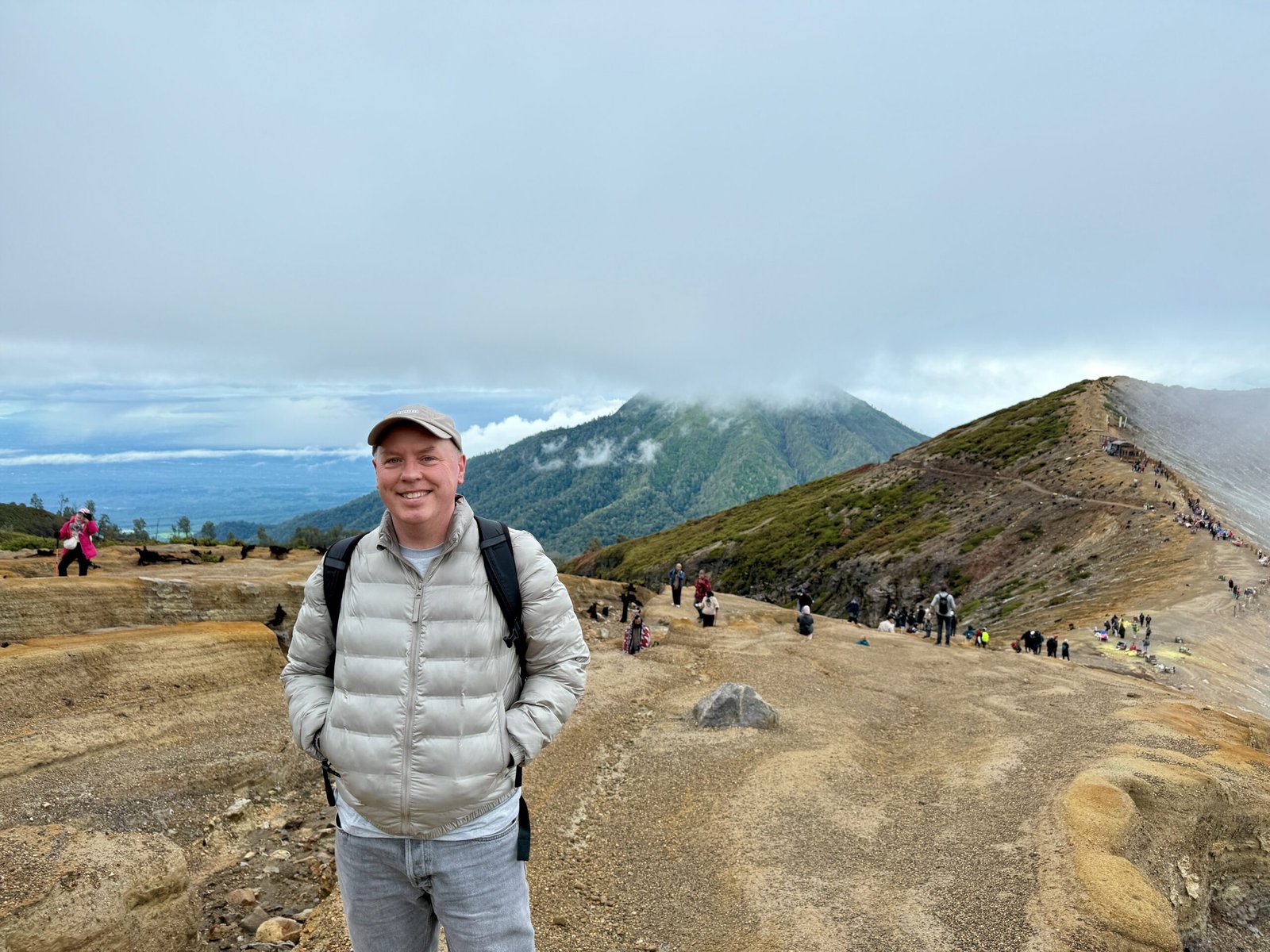 Don Trynor, author of Curious Don, stands on the summit rim of Ijen Volcano with Banyuwangi in the distance, surrounded by fellow hikers.