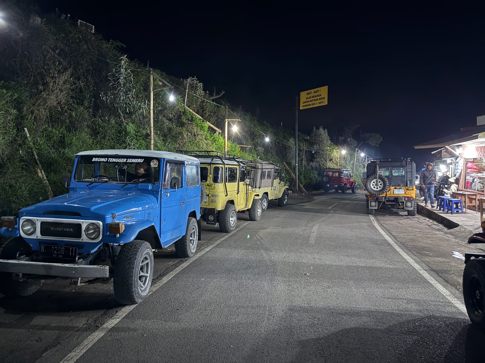 Jeeps parked at the Bukit Cinta basecamp with tourists eating noodles, bean curds, and sipping coffee as they wait for sunrise near Mount Bromo.