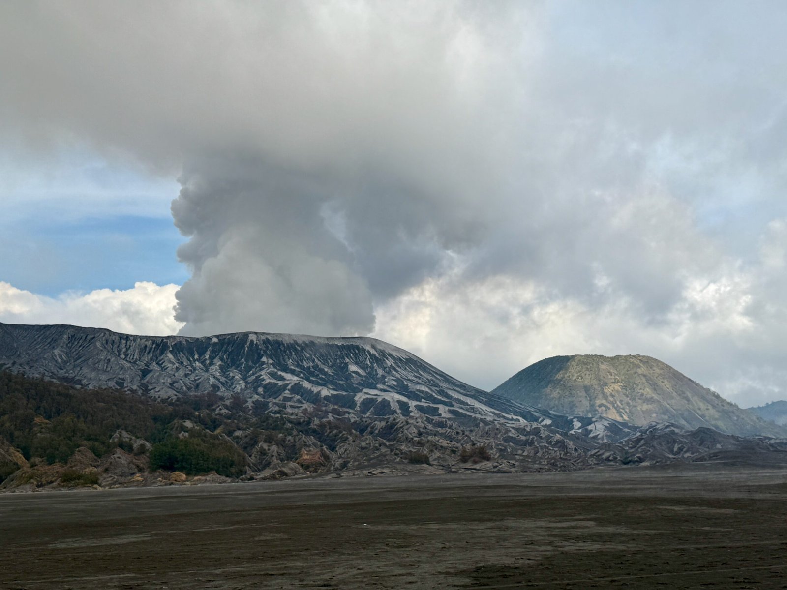 Mount Bromo with smoke and steam rising from its caldera on the left and Mount Batok on the right, viewed from the floor of the Tengger Caldera.