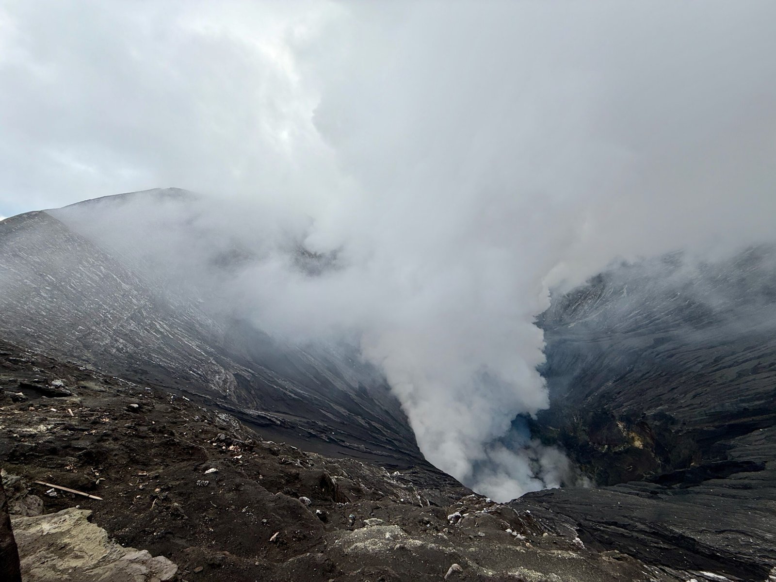 View from the rim of Mount Bromo’s caldera, looking into its smoking and steaming crater with sulfuric gases rising toward the sky.