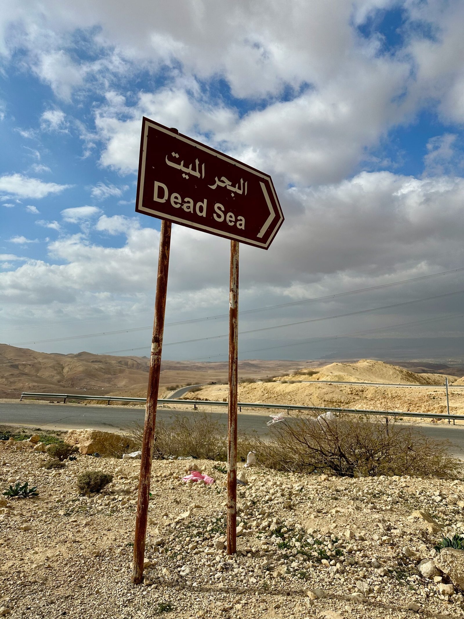 Road sign pointing towards the Dead Sea from Mount Nebo, with the Dead Sea visible on the horizon in the distance.