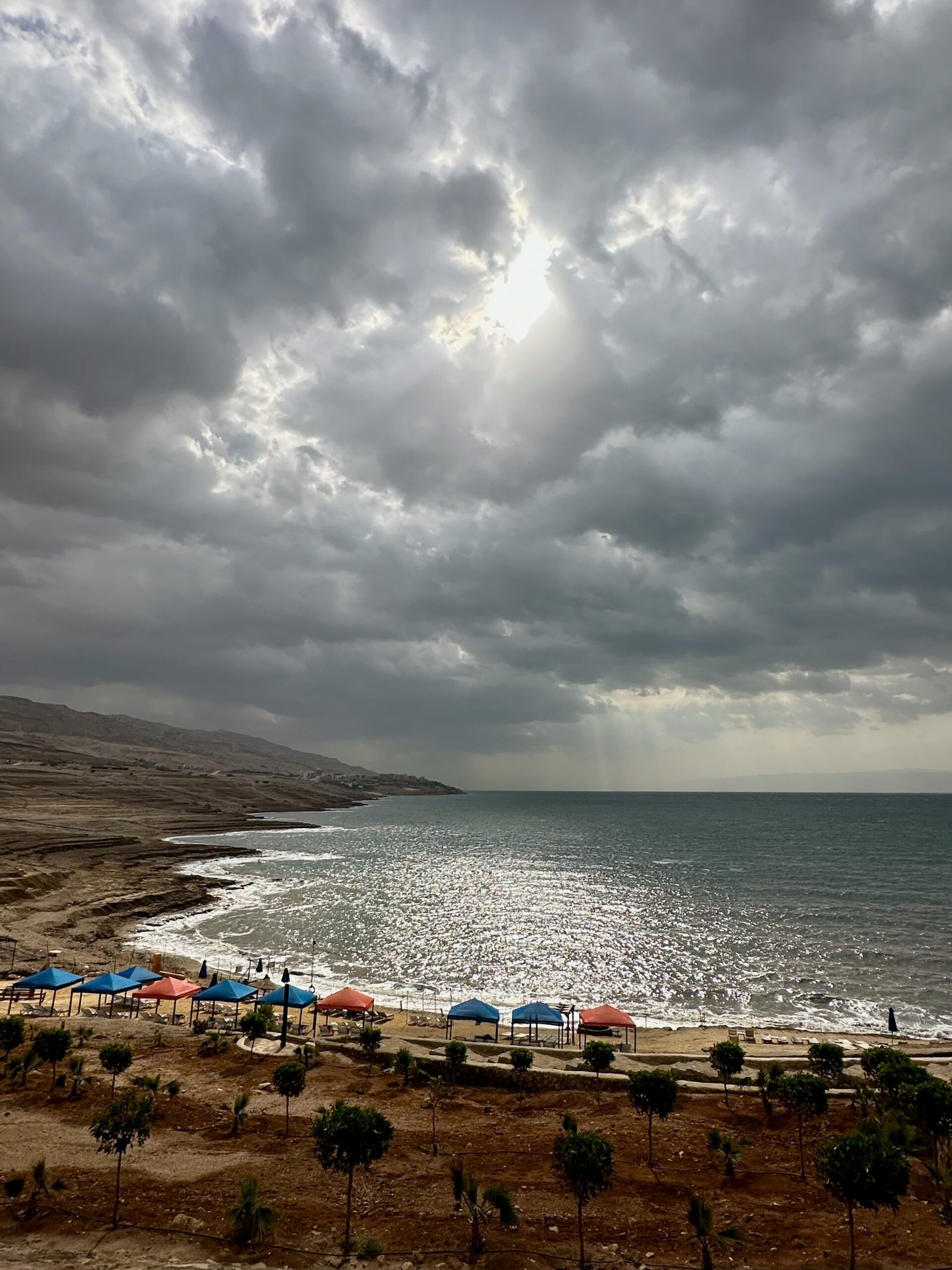 View from a hillside of a private beach and the Dead Sea at a resort in Swemeh, Jordan, facing south with clear waters and a peaceful shoreline.